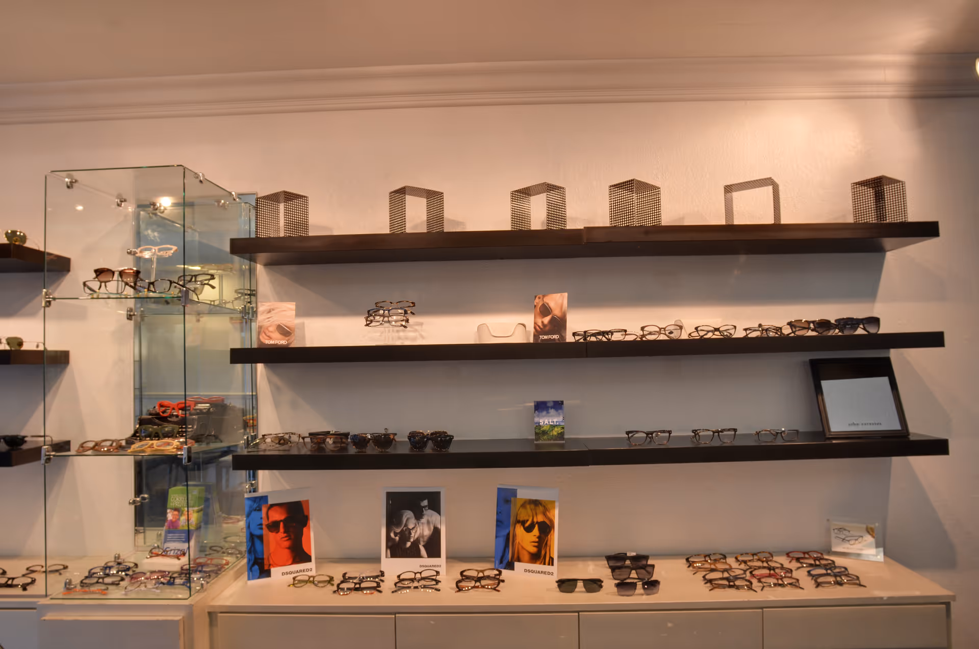 Display of numerous eyeglasses arranged on dark shelves and a glass cabinet.