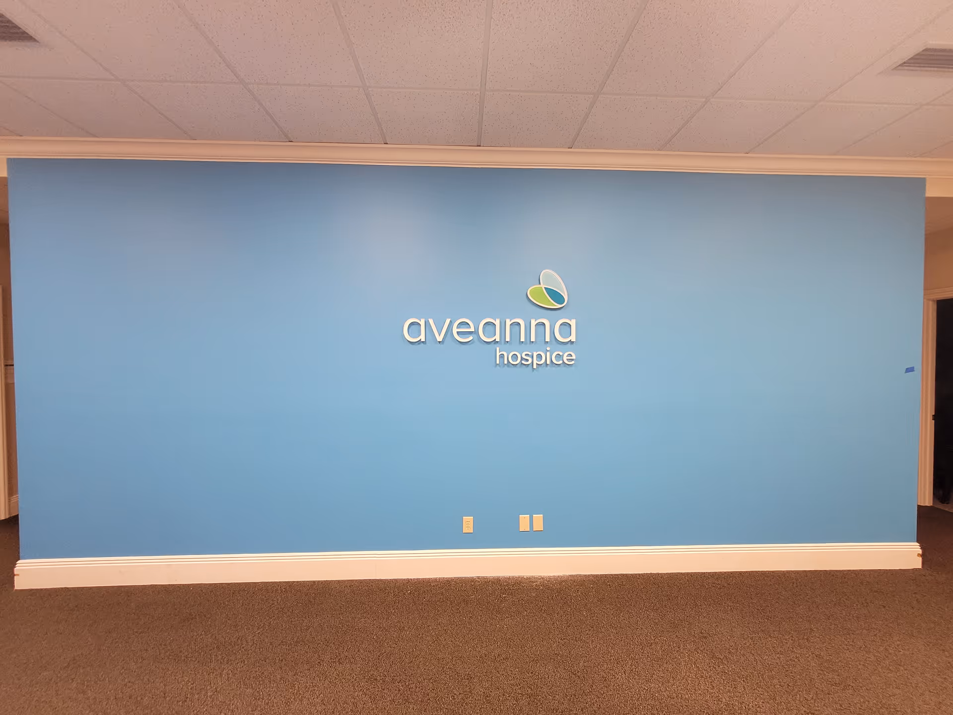 Blue wall with Aveanna Hospice logo in an interior facility lobby.