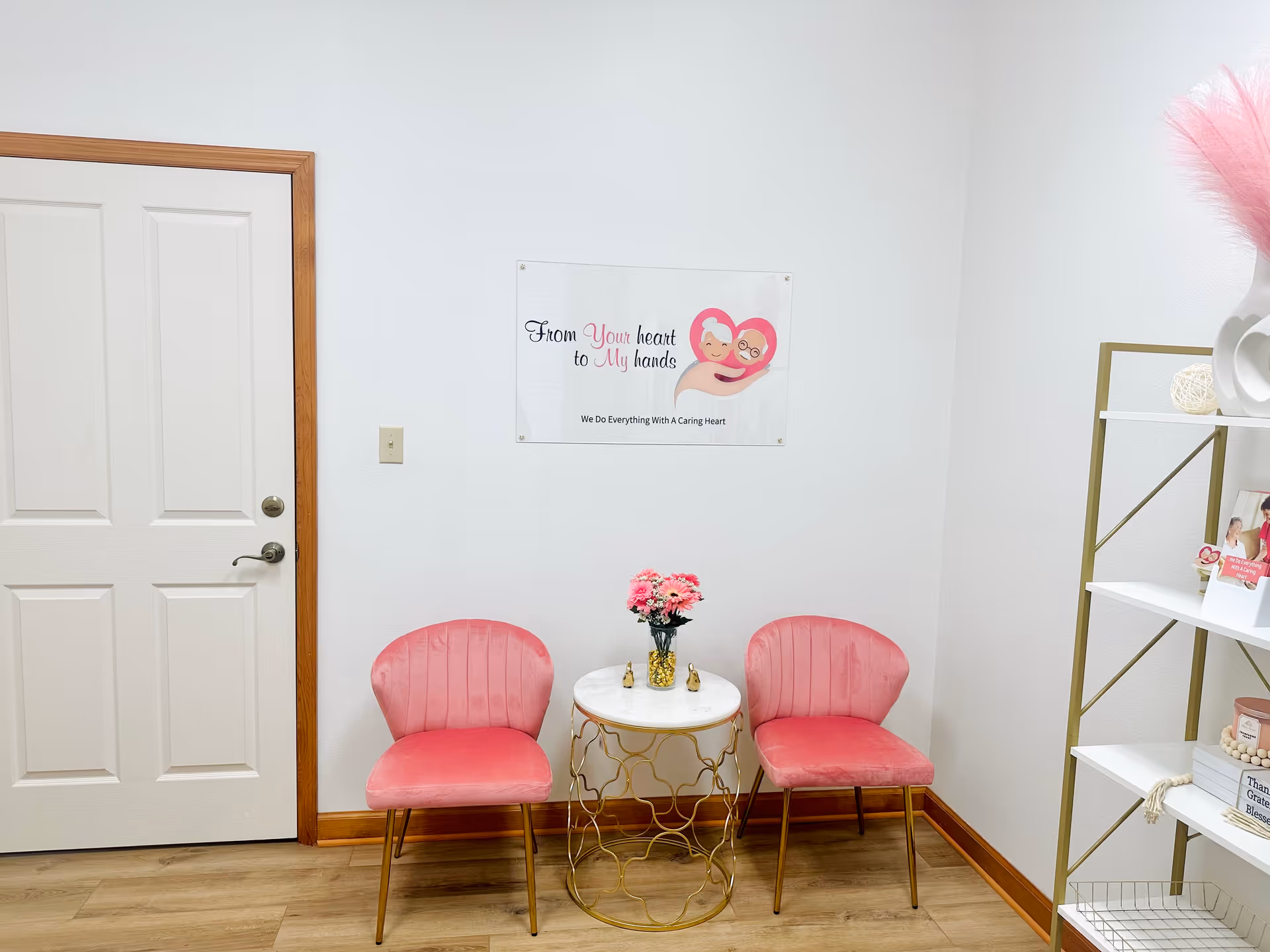 A small corner seating area with two pink chairs, a round table, and a sign.