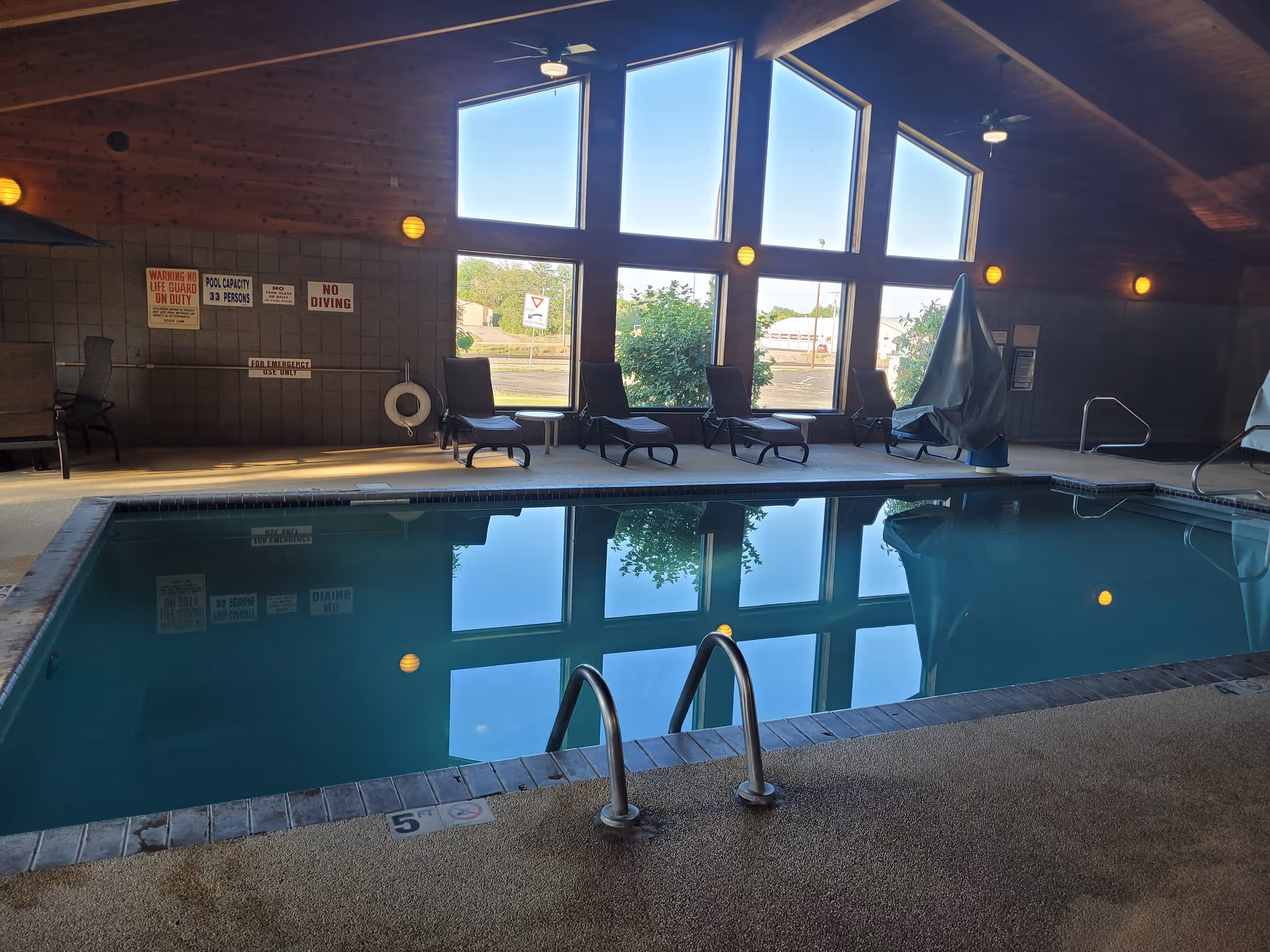 Indoor swimming pool area with loungers along the wall and large windows.