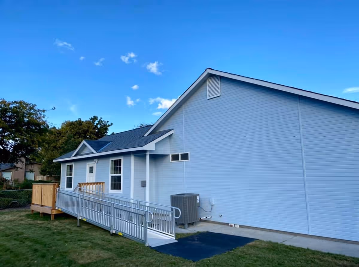 Light blue single-story facility with a wheelchair ramp and small deck, under a clear blue sky.