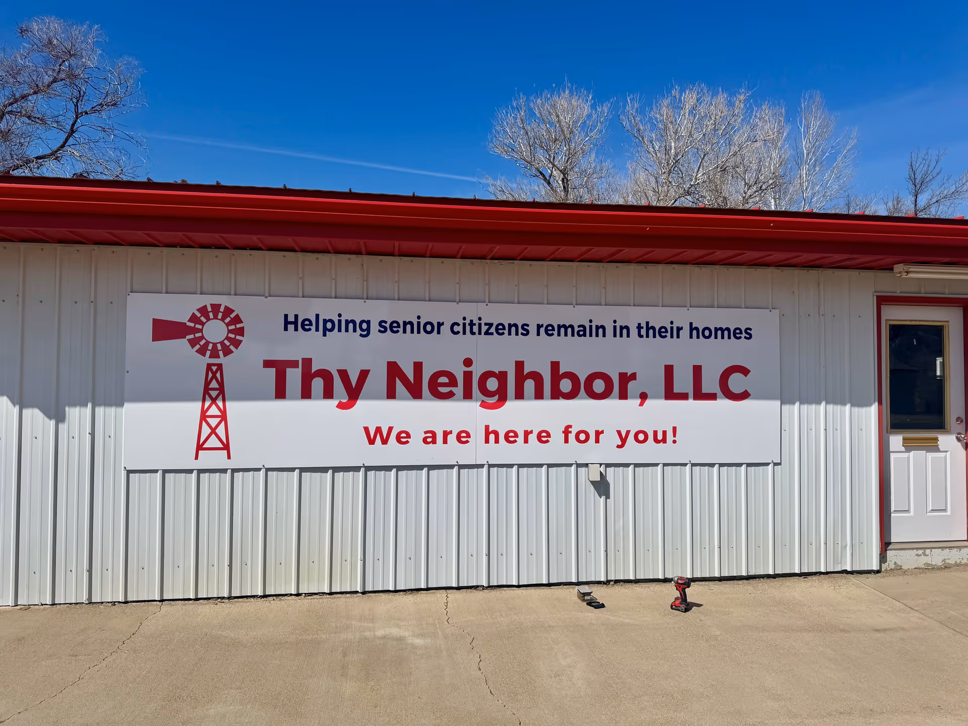 Exterior of a metal building with a large Thy Neighbor, LLC sign and a door.