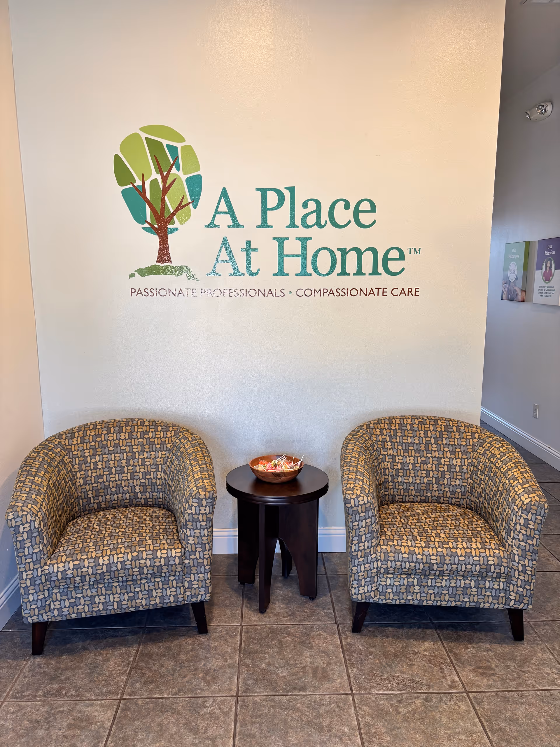 Lobby seating area with two patterned chairs and a small table beside the facility logo