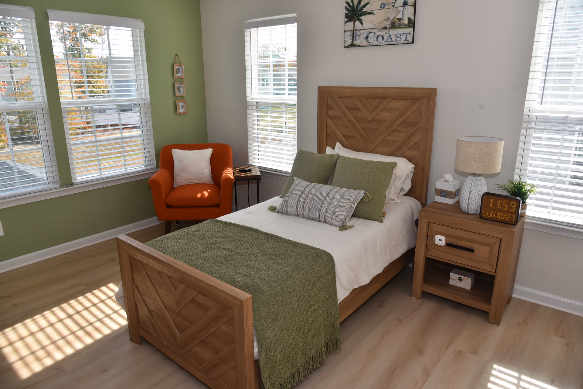 A cozy bedroom with a wooden bed, green accents, an orange chair, and a nightstand.
