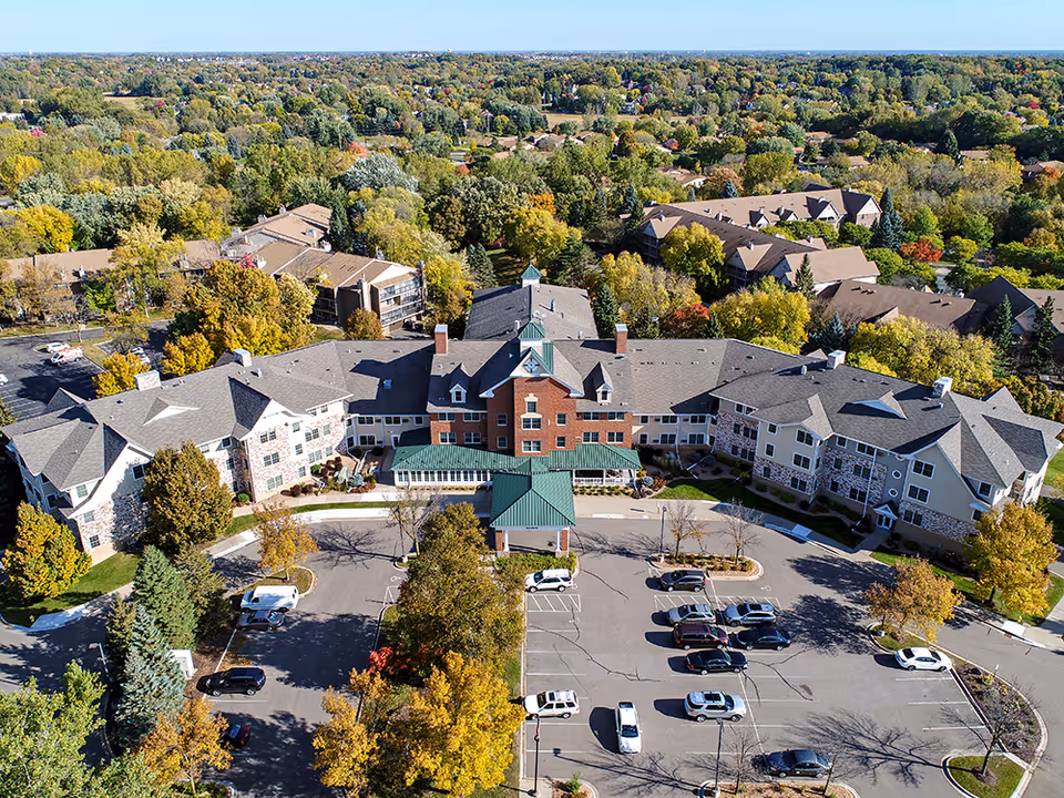 Aerial view of the Plymouth Towne Square senior living building and parking lot surrounded by trees in autumn.