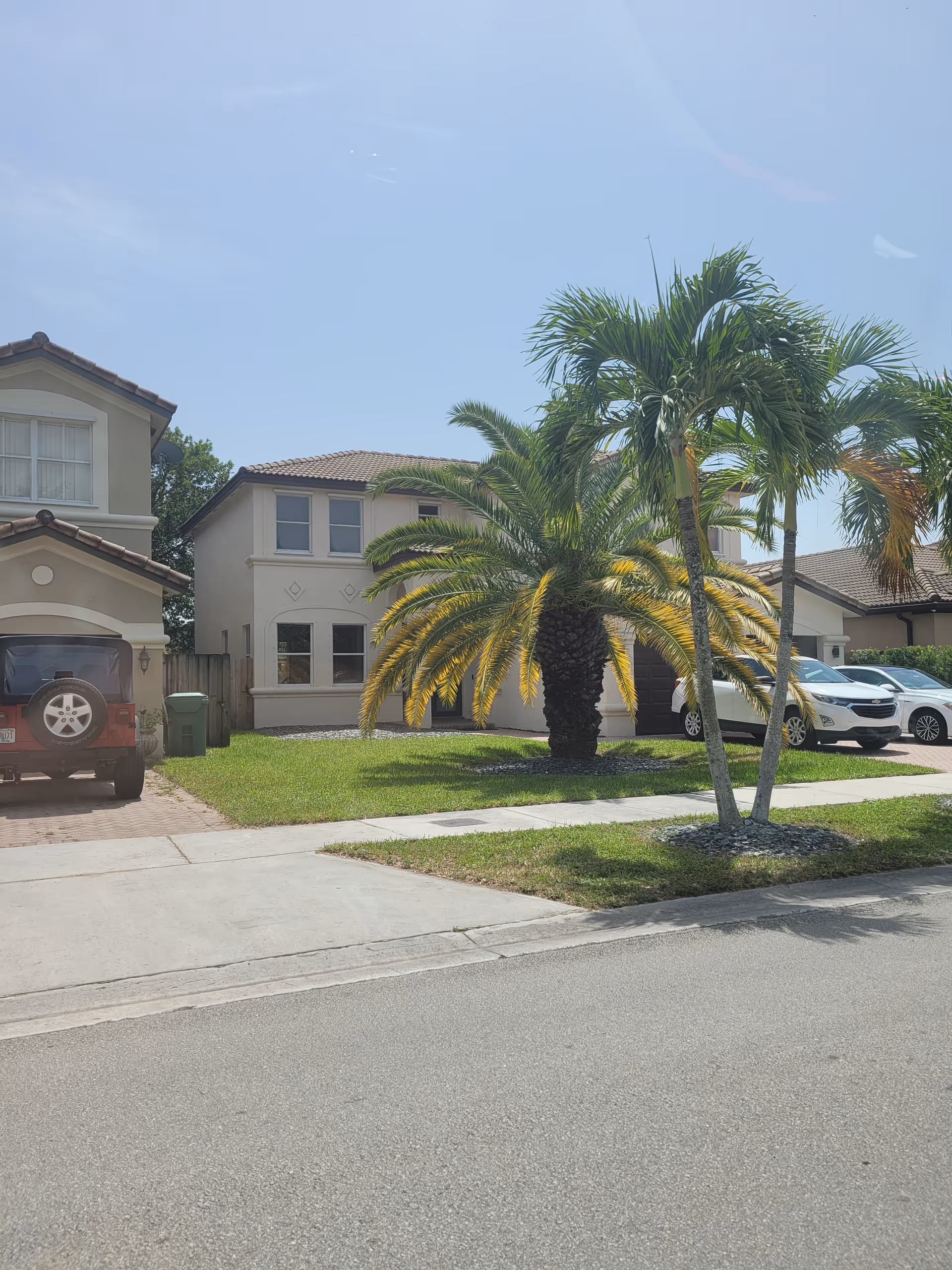 Front view of a beige residential building with palm trees and parked cars.