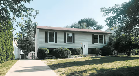 A single-story residential home with a front yard, driveway, and trimmed shrubs.