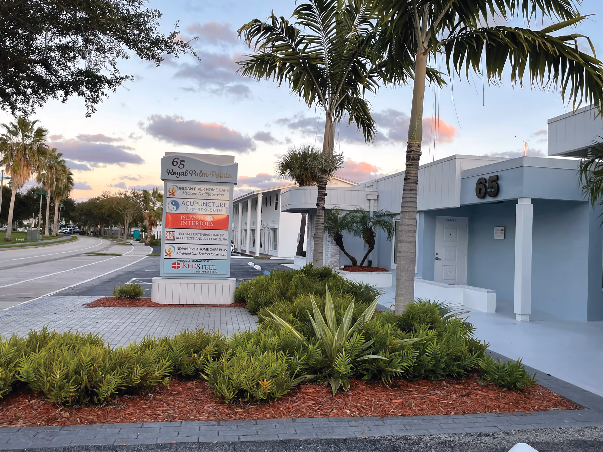 Exterior view of a light-blue building with palm trees and a front sign.