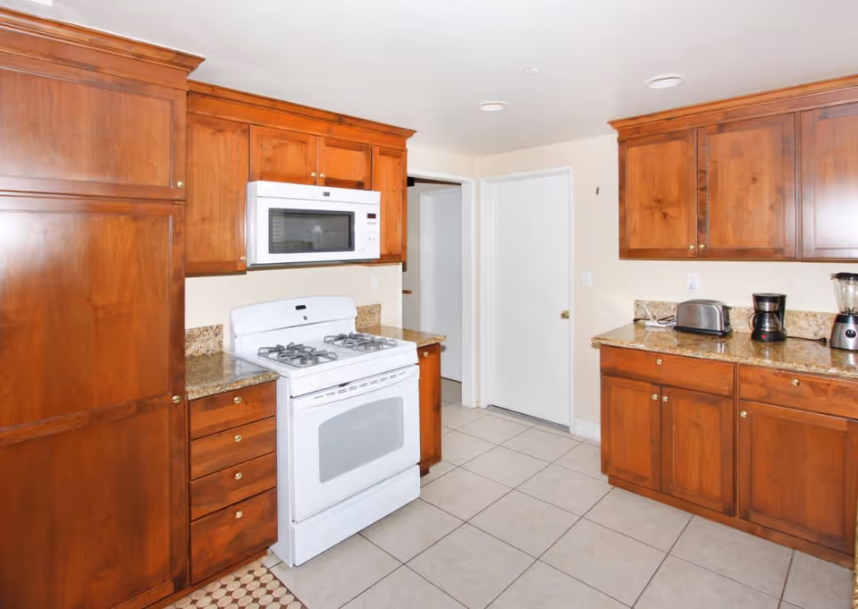 Bright kitchen with wooden cabinets, white appliances, and granite countertops.