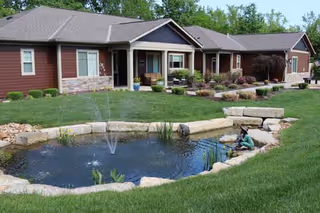 Single-story Bridge Haven Village exterior with landscaped yard and a small pond in front.