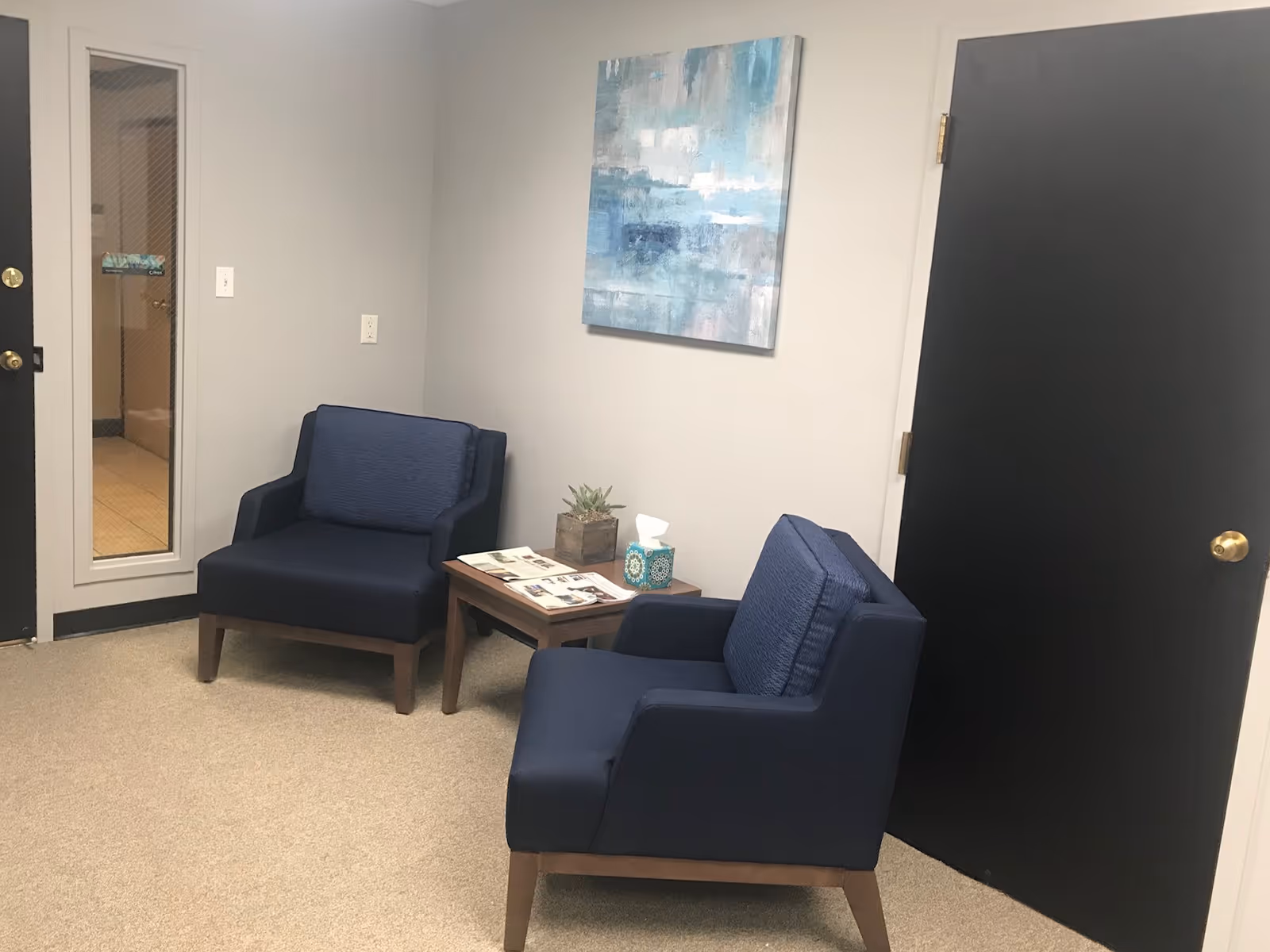 Two blue chairs with a small table in a neutral lounge area.