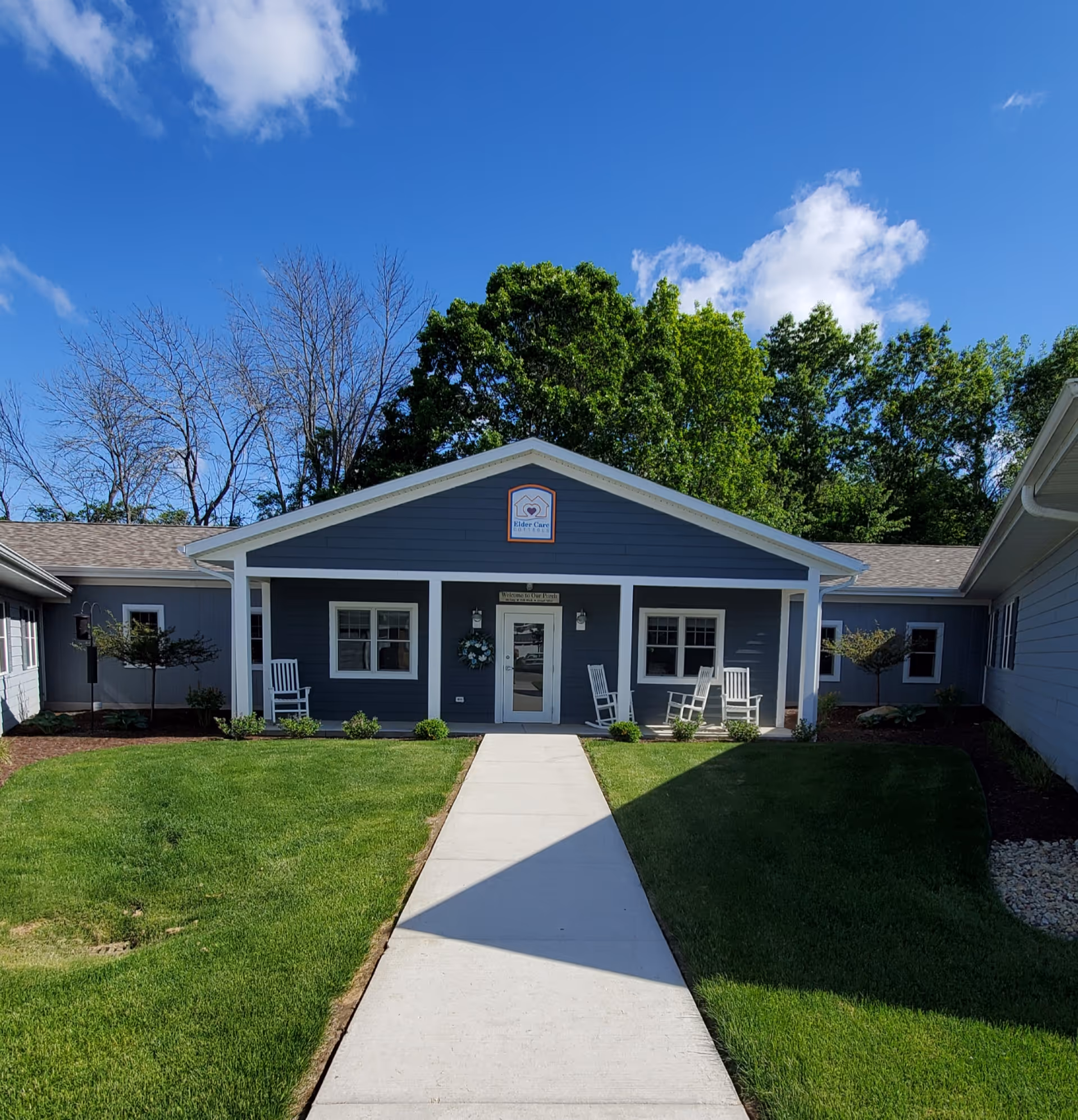 Blue, single-story senior living building with a front porch and rocking chairs.