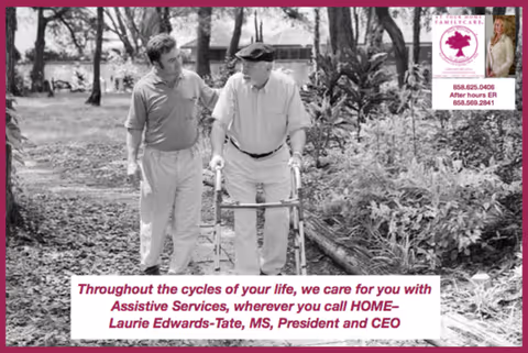 A caregiver walks outdoors assisting an elderly man using a walker along a garden path.