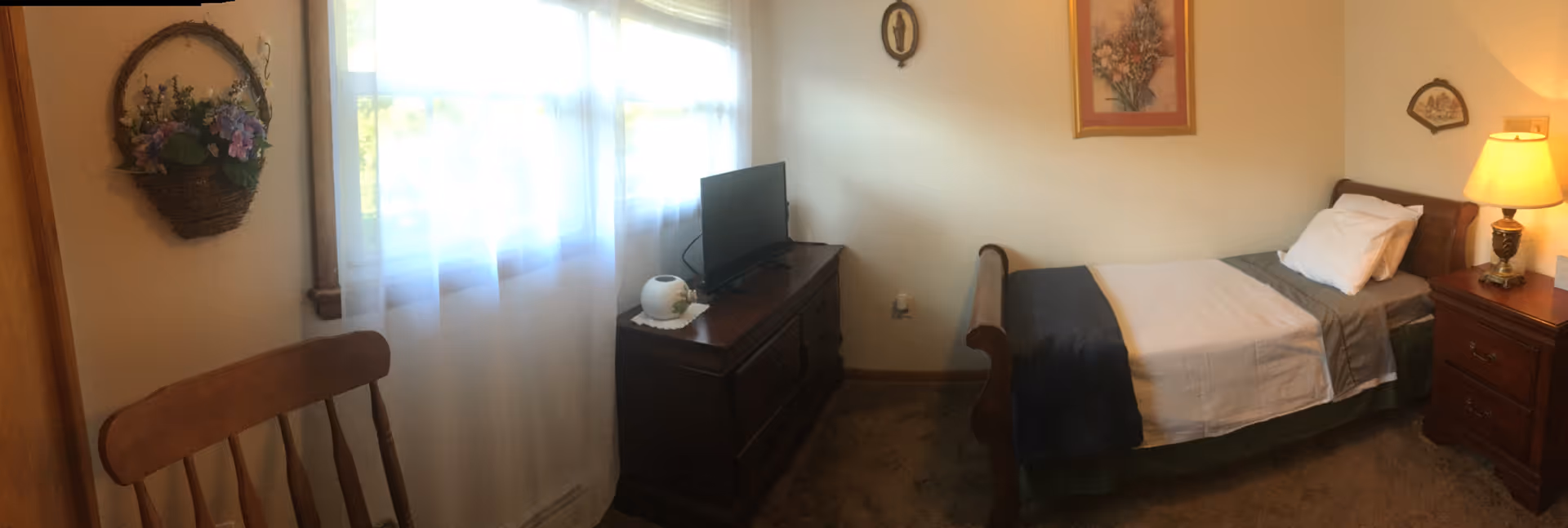 A cozy senior living bedroom with a single bed, dresser, TV, and window.