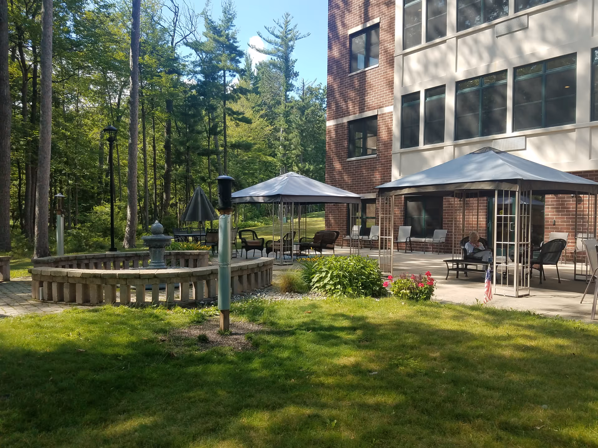 Outdoor patio at Point Manor Assisted Living with canopied seating, a fountain, and a brick building.