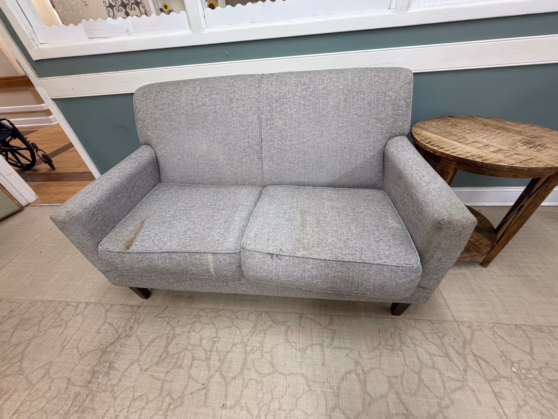 Gray loveseat and wooden side table in a memory care facility living room.