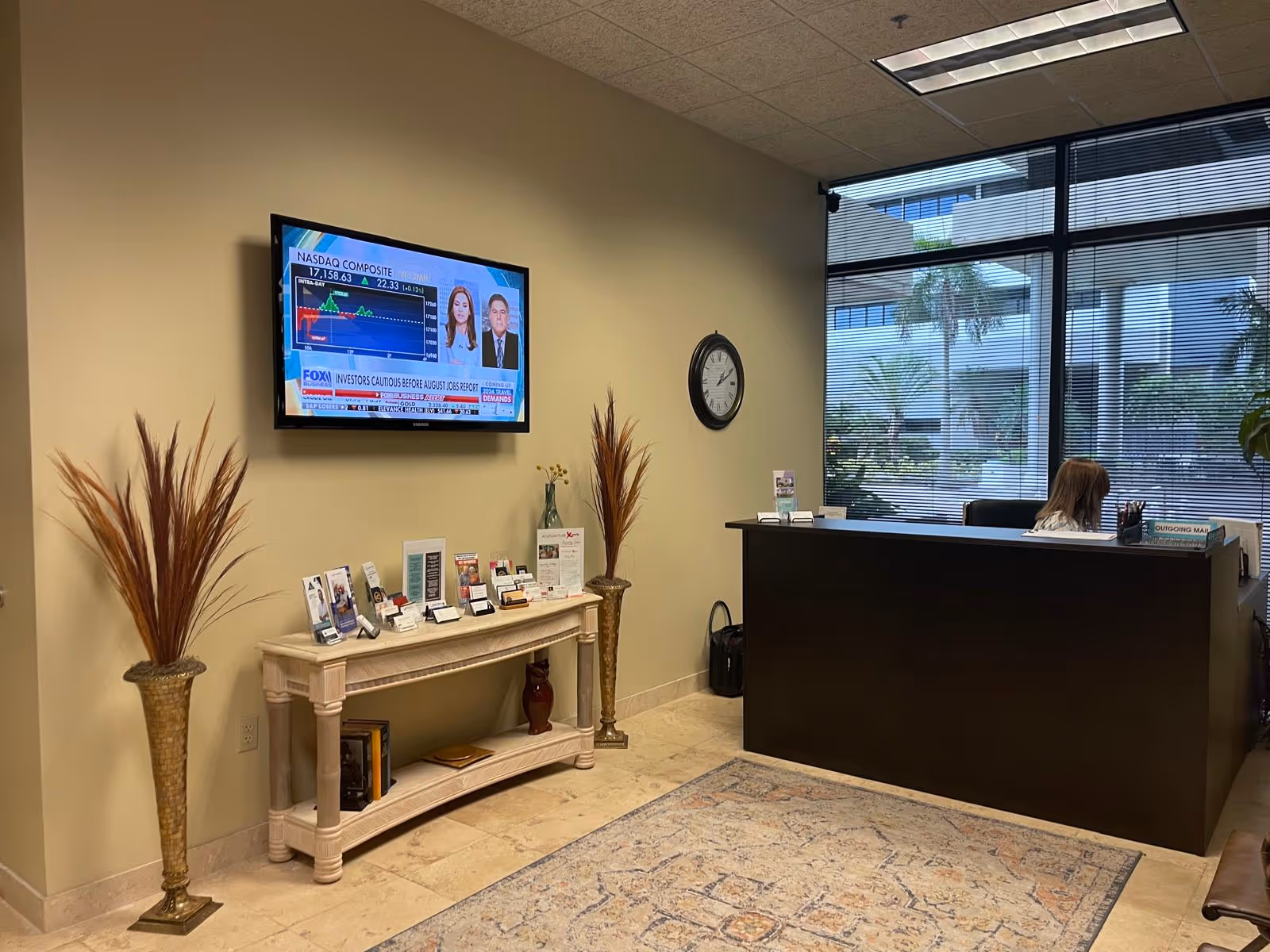 Reception area of a senior living facility with a desk, wall TV, brochures, and plants.