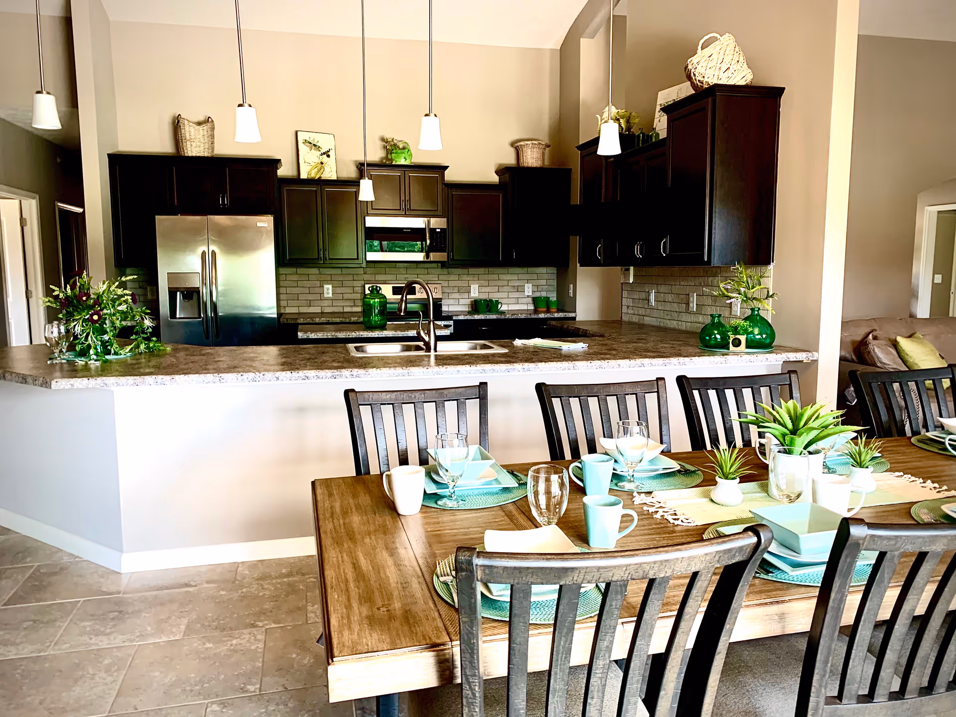 Open-concept kitchen with dark cabinets, island, pendant lights, and a dining table setup.