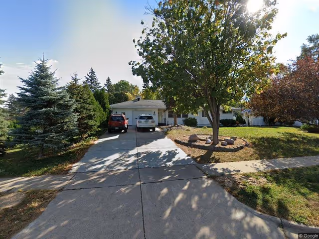 Front view of a single-story suburban house with a driveway, two parked cars, and a tree in the yard.