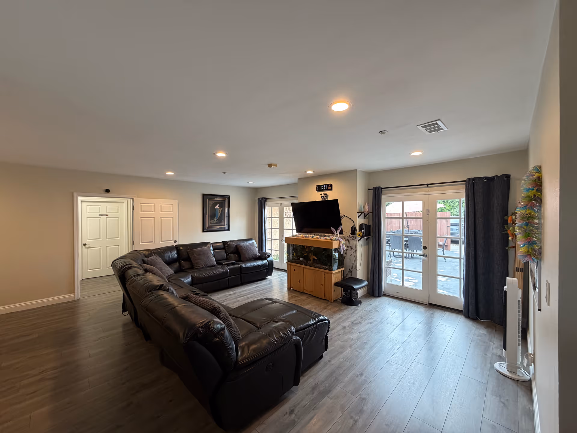 Spacious living room with black leather sectional, TV on stand, and glass doors to patio.