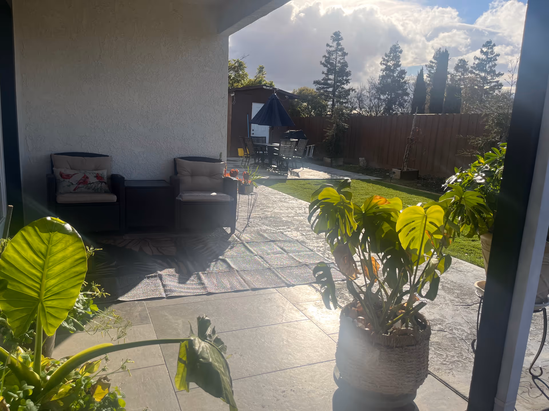 Outdoor patio with seating, potted plants, an umbrella table, and a grassy backyard.