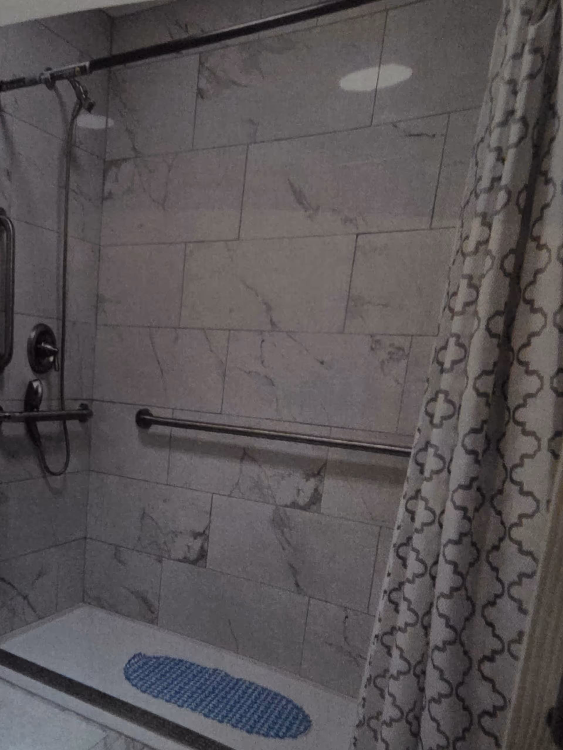 Senior living facility bathroom with marble tiles, grab bar, and patterned shower curtain.