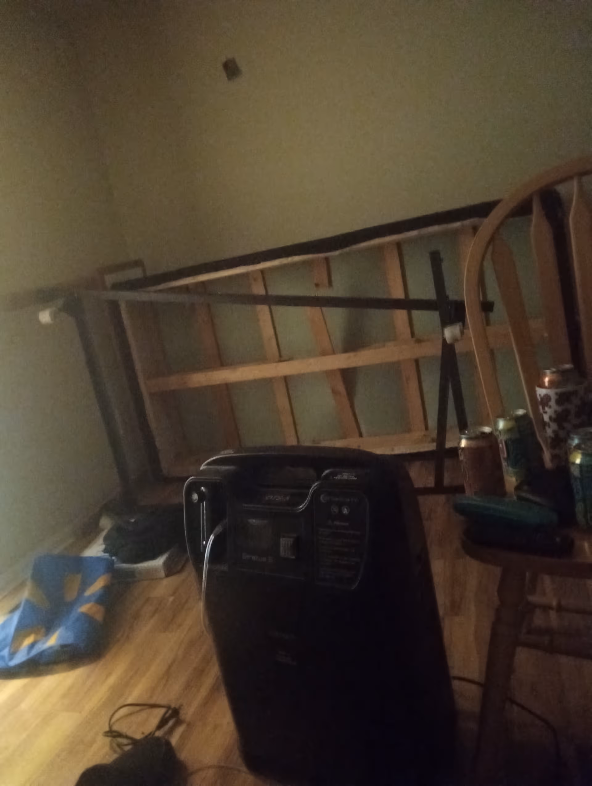 Dimly lit interior with a toppled bed frame, heater, and cluttered table.