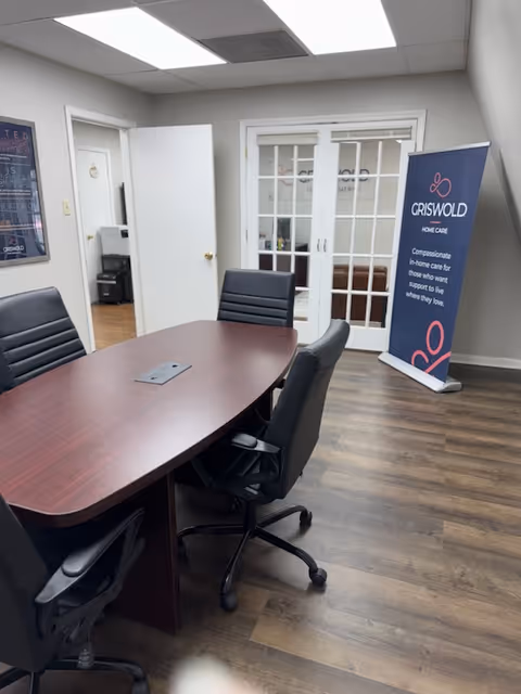 Conference room with dark wood table, black chairs, and a Griswold Home Care banner.