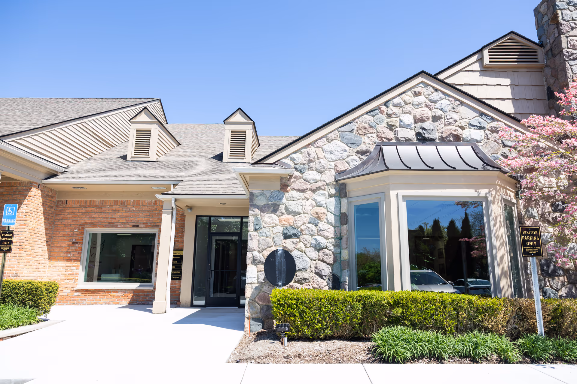 Stone-and-brick senior living facility entrance with glass doors and landscaped front yard.