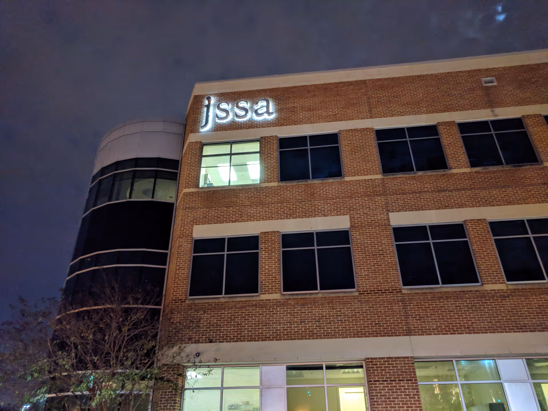Night-time exterior view of a brick building with a lit jssa sign.