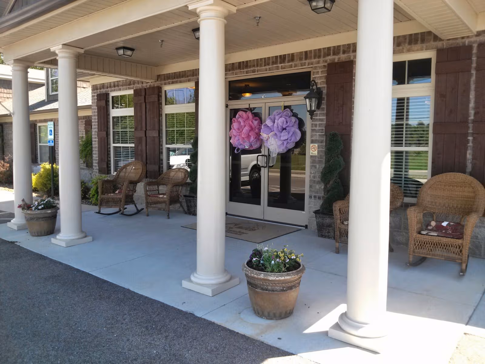 Entrance to Cades Center Assisted Living with columns, seating, and potted flowers.