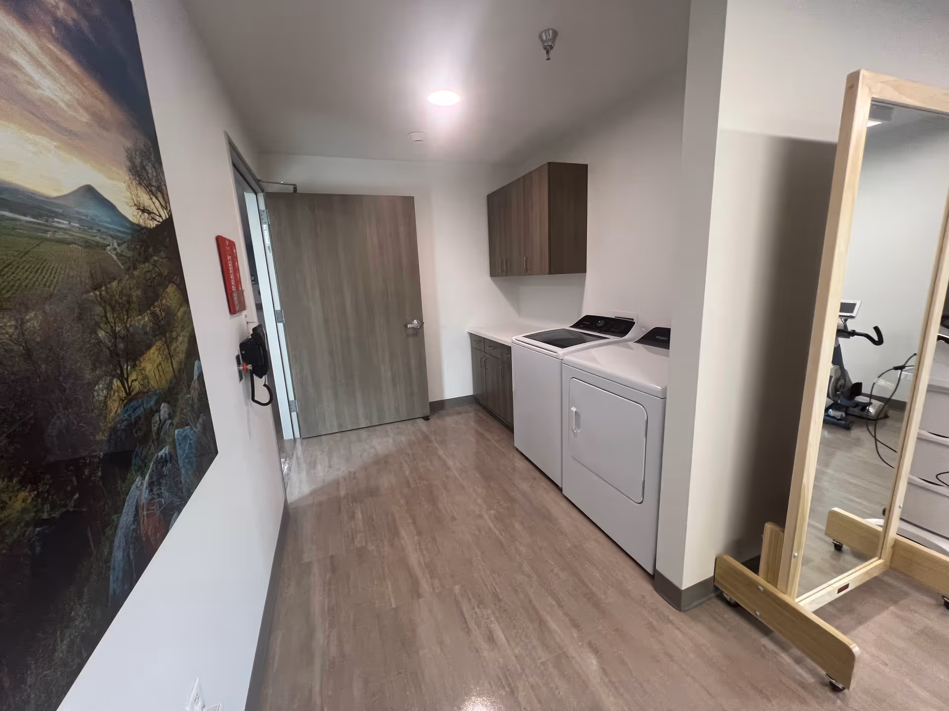 Laundry area with washer, dryer, cabinets, wall mural, and free-standing mirror.