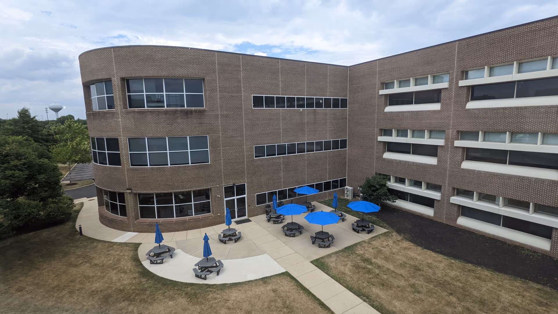 Exterior view of a brick senior living building with outdoor patio and blue umbrellas.