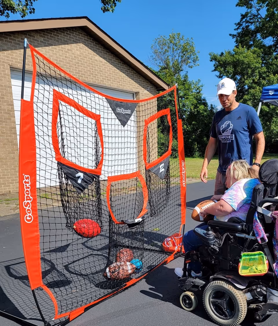 Caregiver and resident in a wheelchair play with a portable outdoor basketball net.