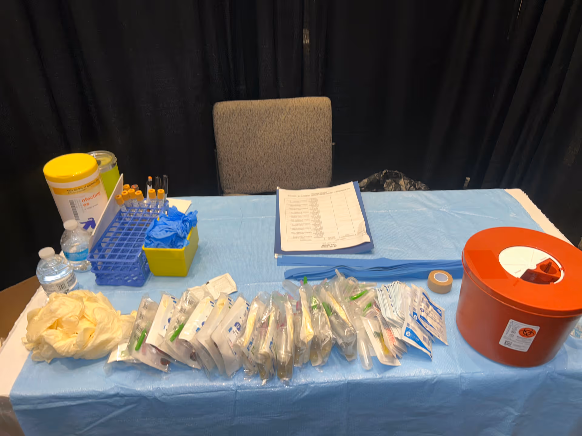 Indoor phlebotomy station on a blue table cover with medical supplies and a red biohazard container.