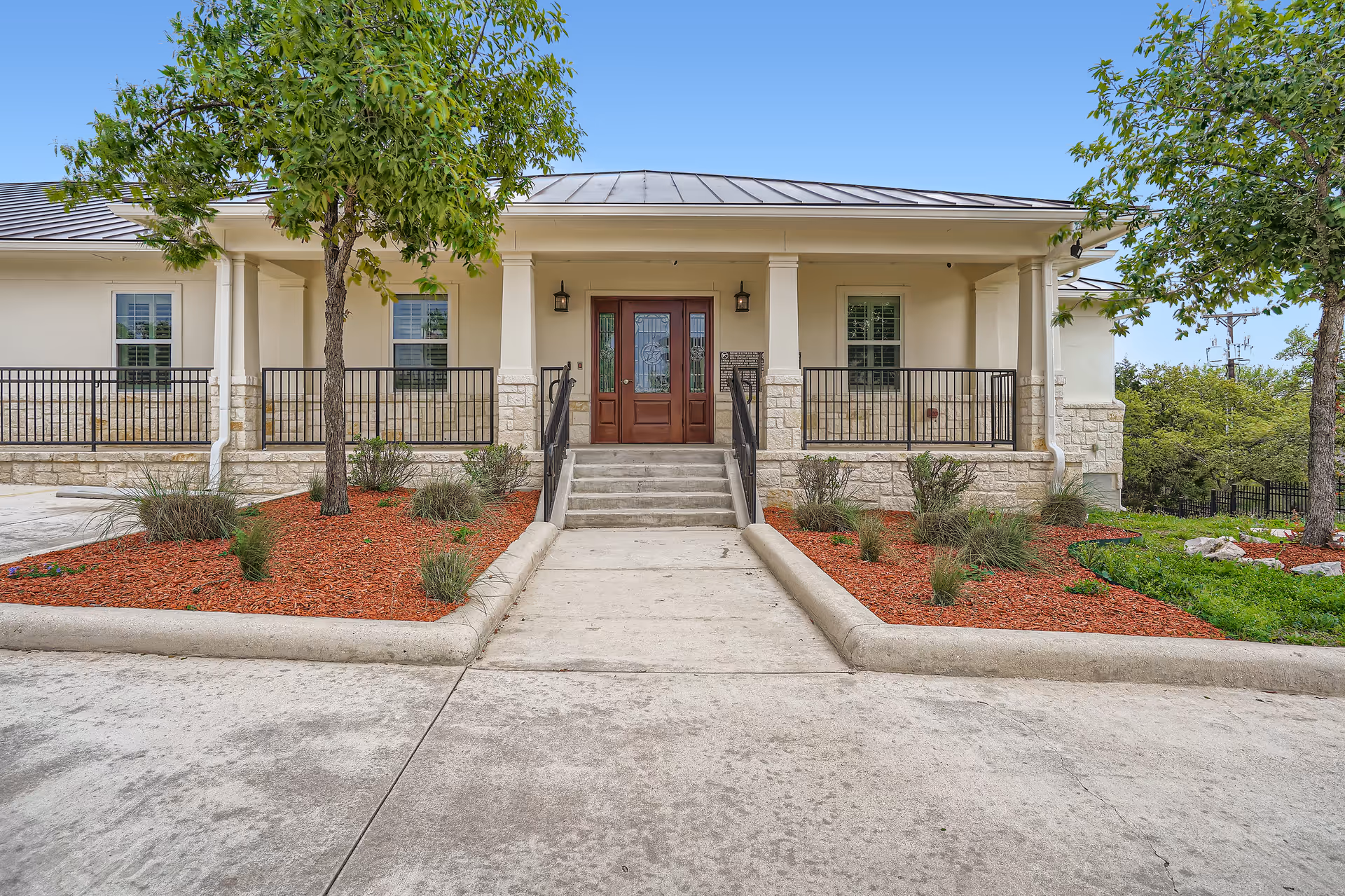 Front entrance of a senior living facility with steps, railing, and landscaped surroundings.