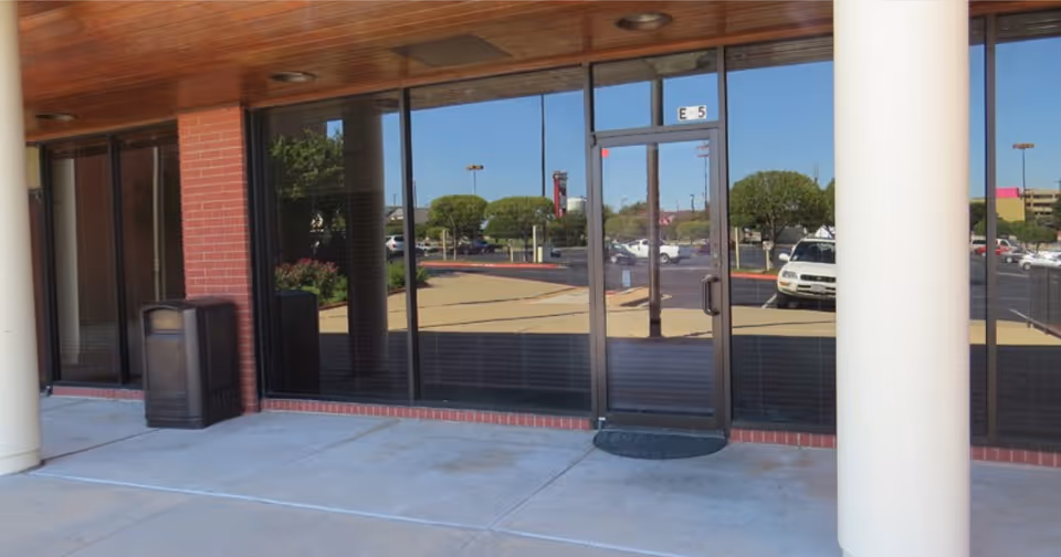 Glass storefront entrance of a senior living facility with reflections of parked cars