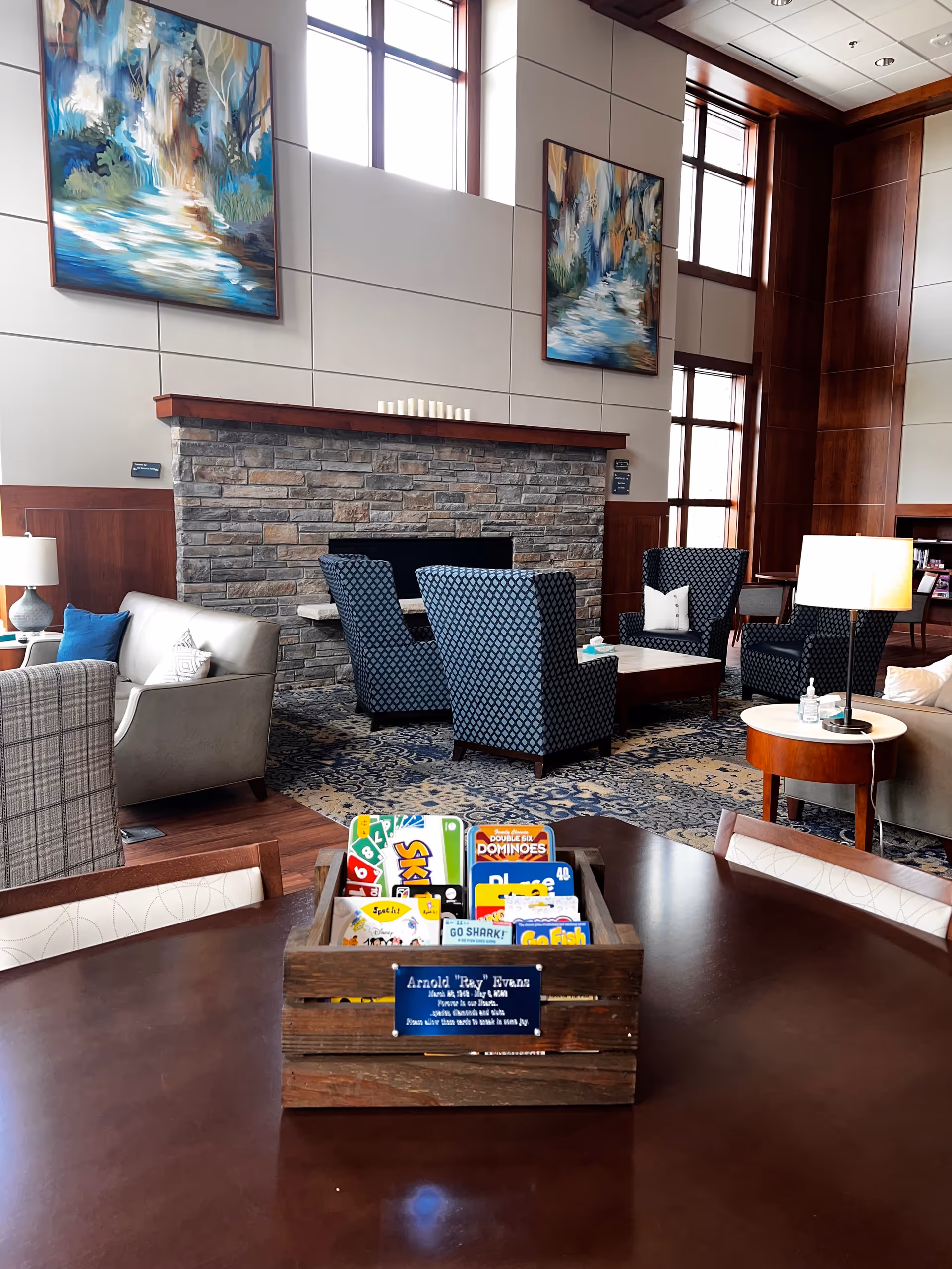 Lobby-style living room in a senior facility with seating around a stone fireplace.