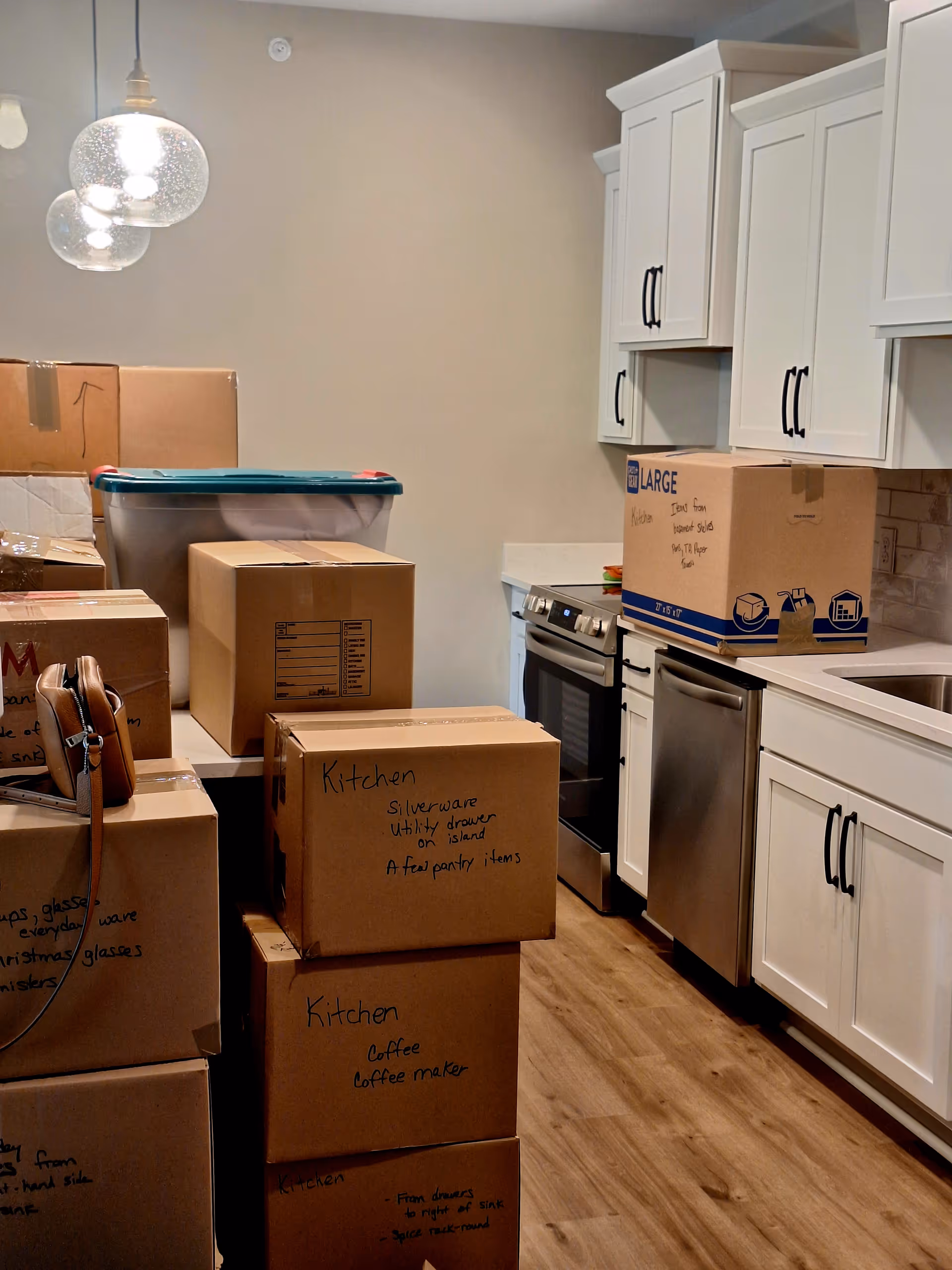A residential kitchen with boxed moving cartons stacked beside cabinets and appliances.