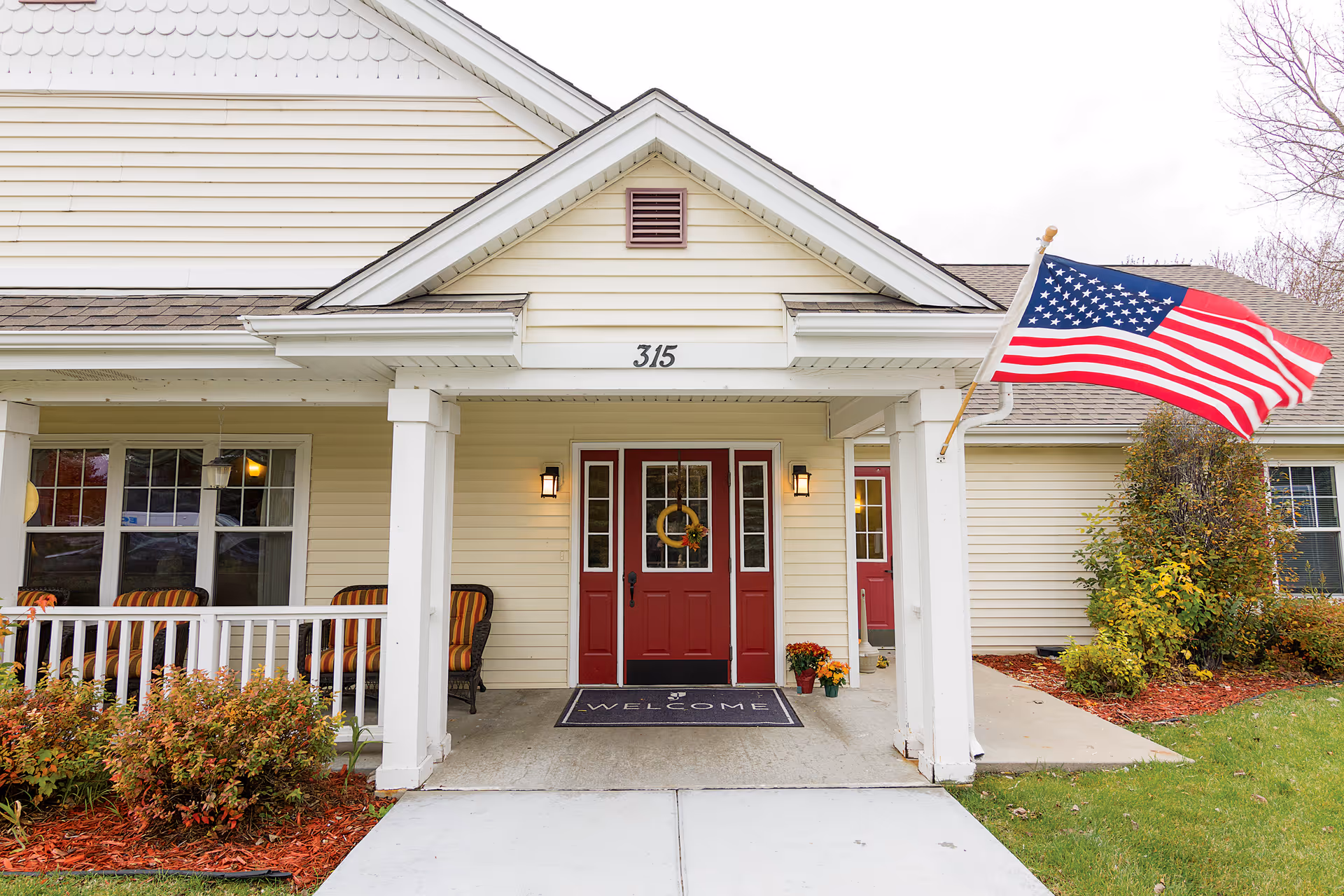 Front entrance of Brookdale West St. Paul with red doors, porch seating, and an American flag.