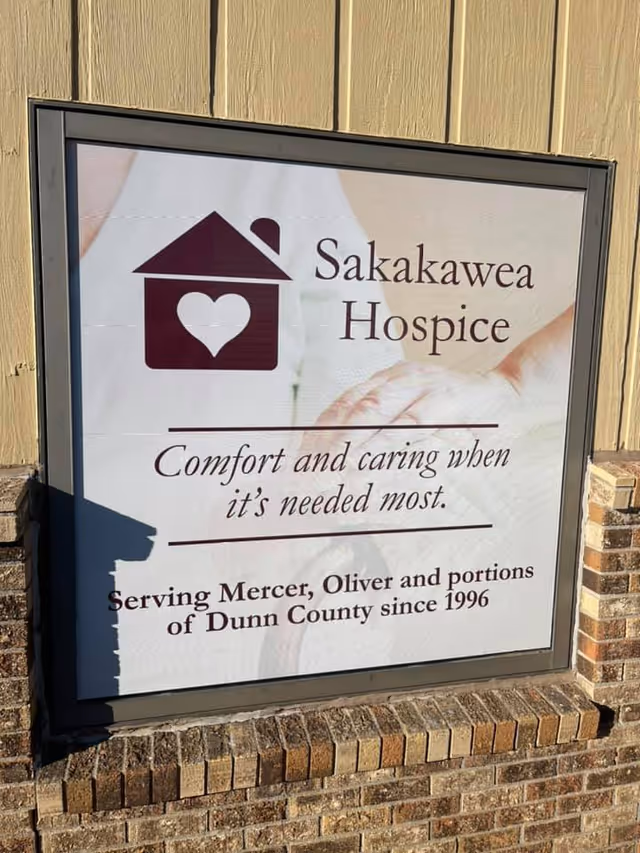 Outdoor sign on a brick building reads Sakakawa Hospice with a heart logo.