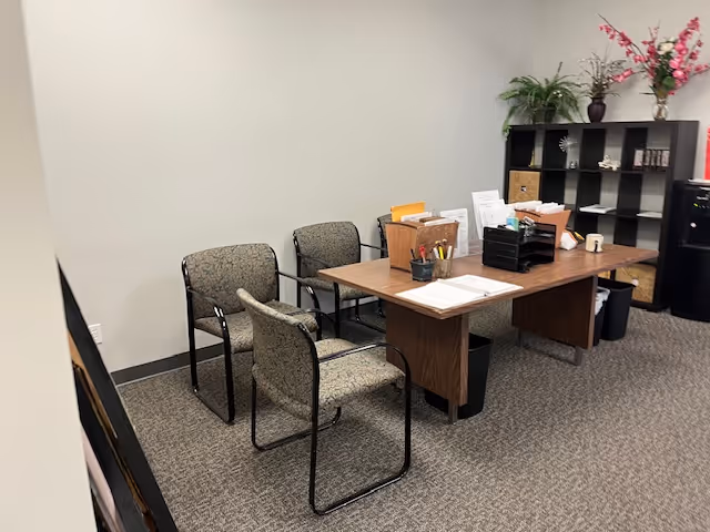 A small office area with a wooden desk, chairs, and filing shelves.