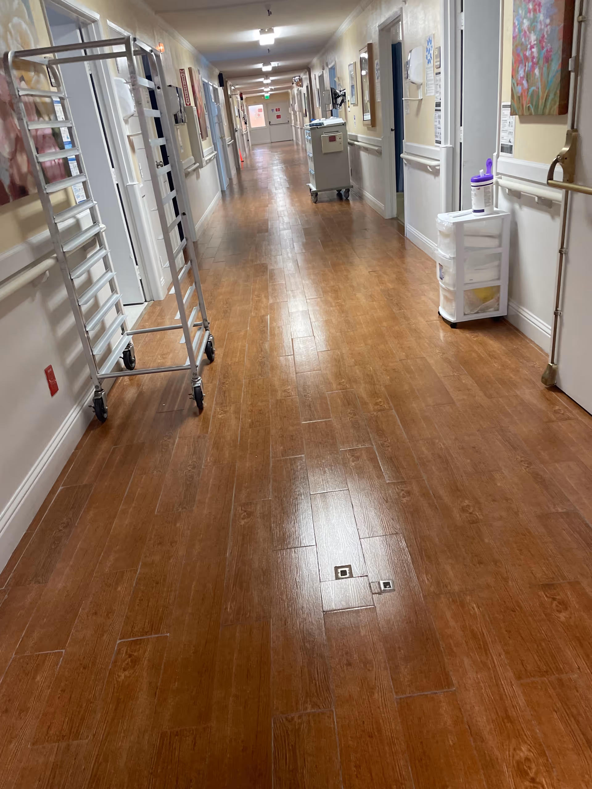 Long indoor hallway with wooden floor, carts, doors, and artwork along walls.