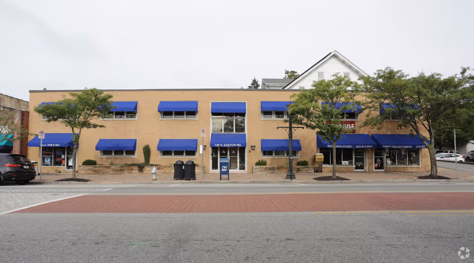Brick storefront building with blue awnings and trees along a street.