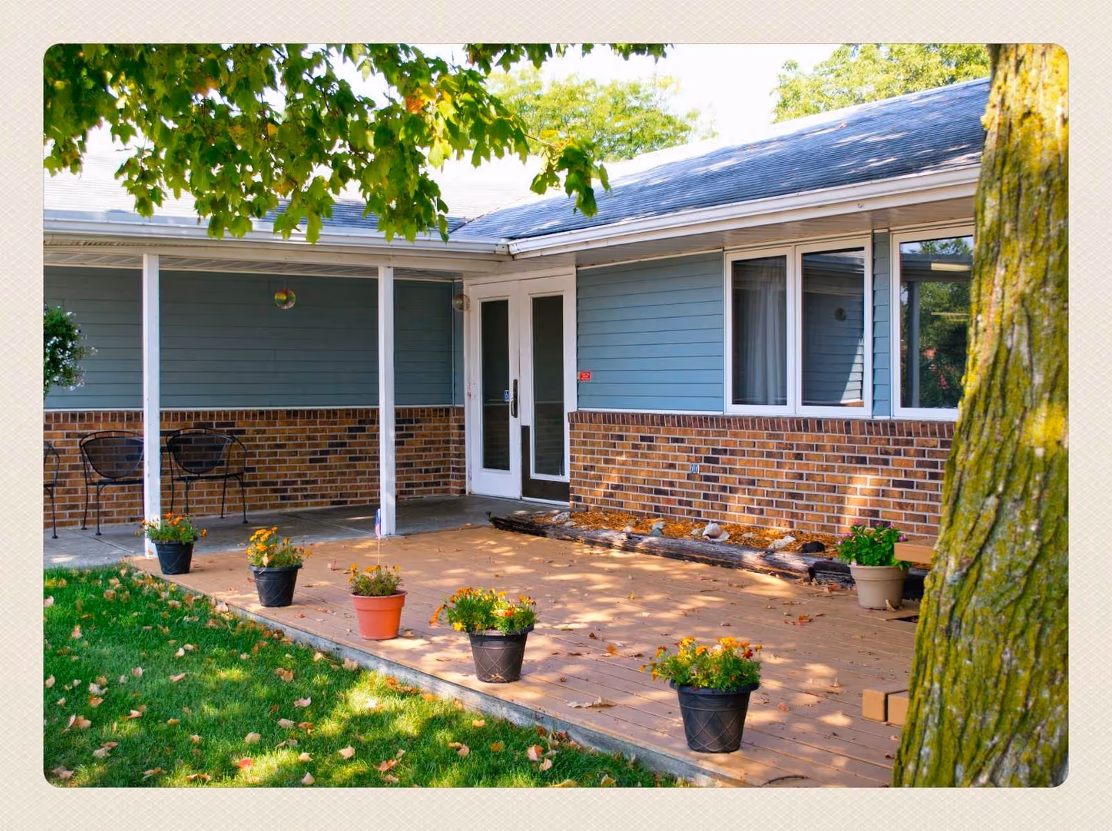 Front porch of Evergreen Estates I with potted plants and seating under trees.