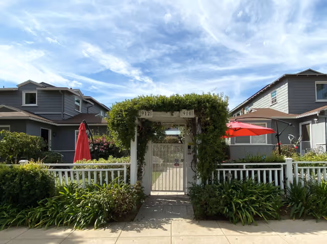 Entrance gate to a residential care facility framed by greenery and red umbrellas