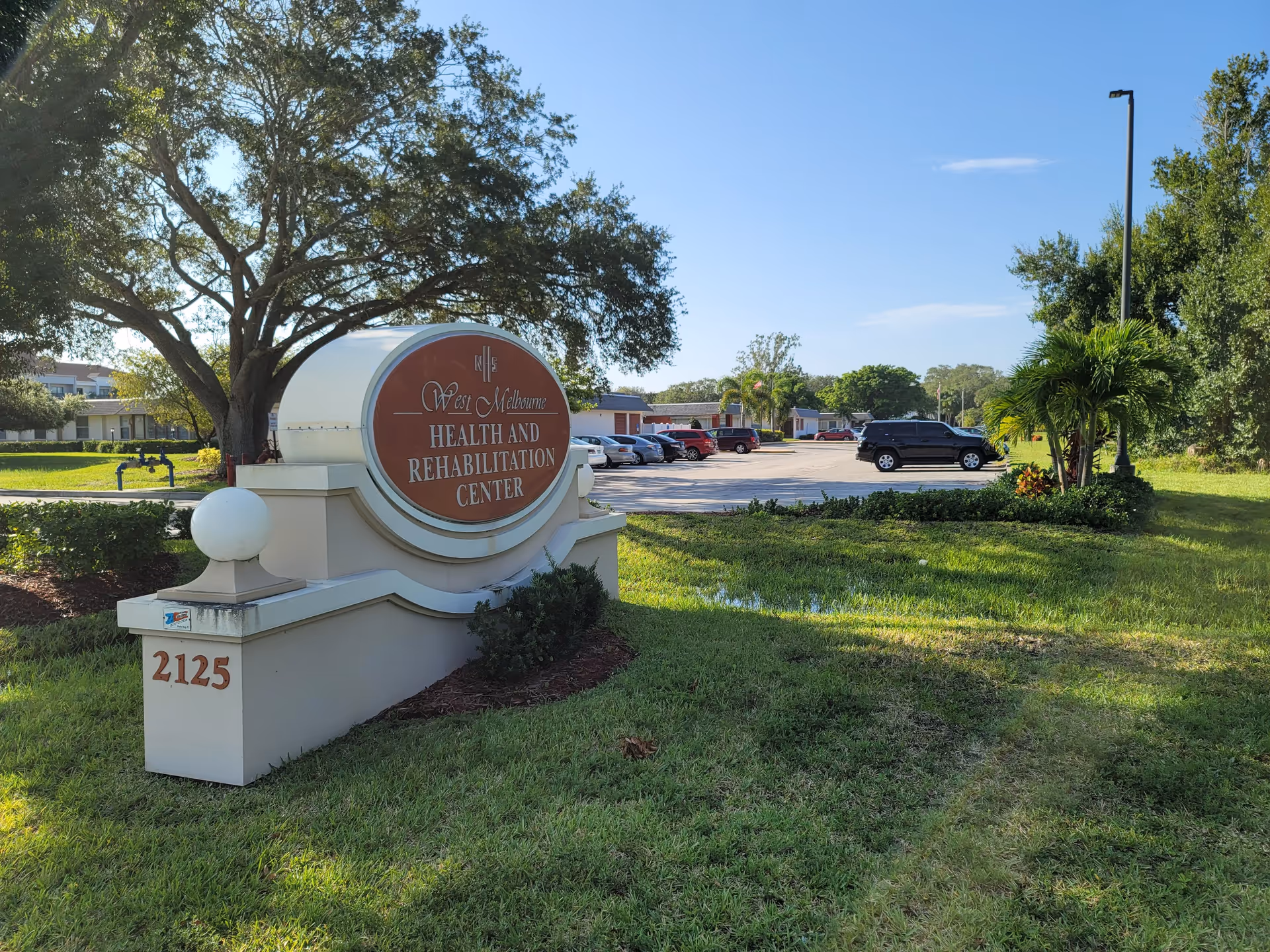 Exterior view of a senior health center sign with parking and green landscaping.