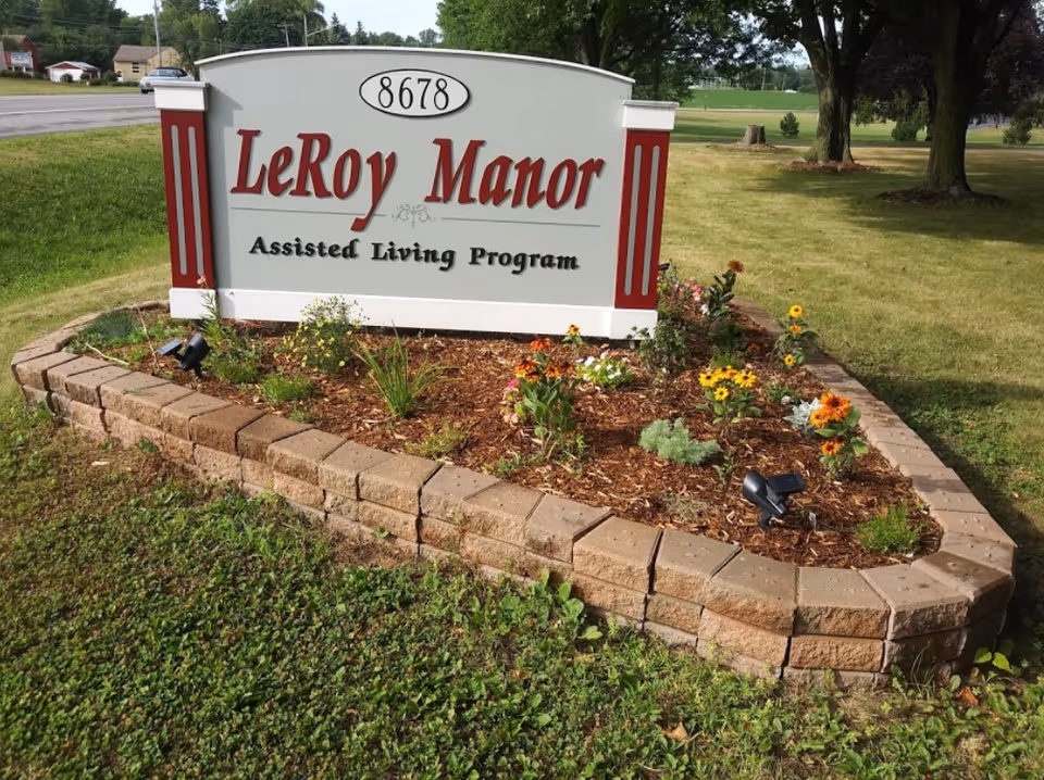 LeRoy Manor sign with a flower bed and trimmed lawn outside the facility.
