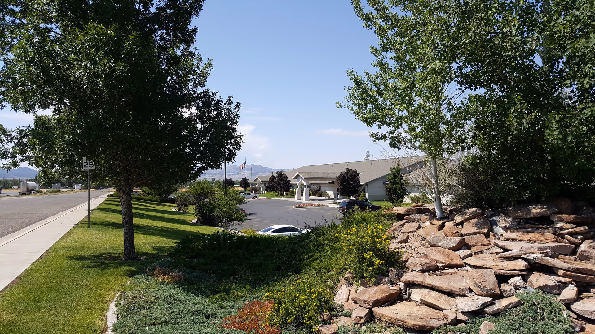 Exterior view of Beaver Valley Hospital grounds with trees, rock garden, sidewalk, and parking lot.
