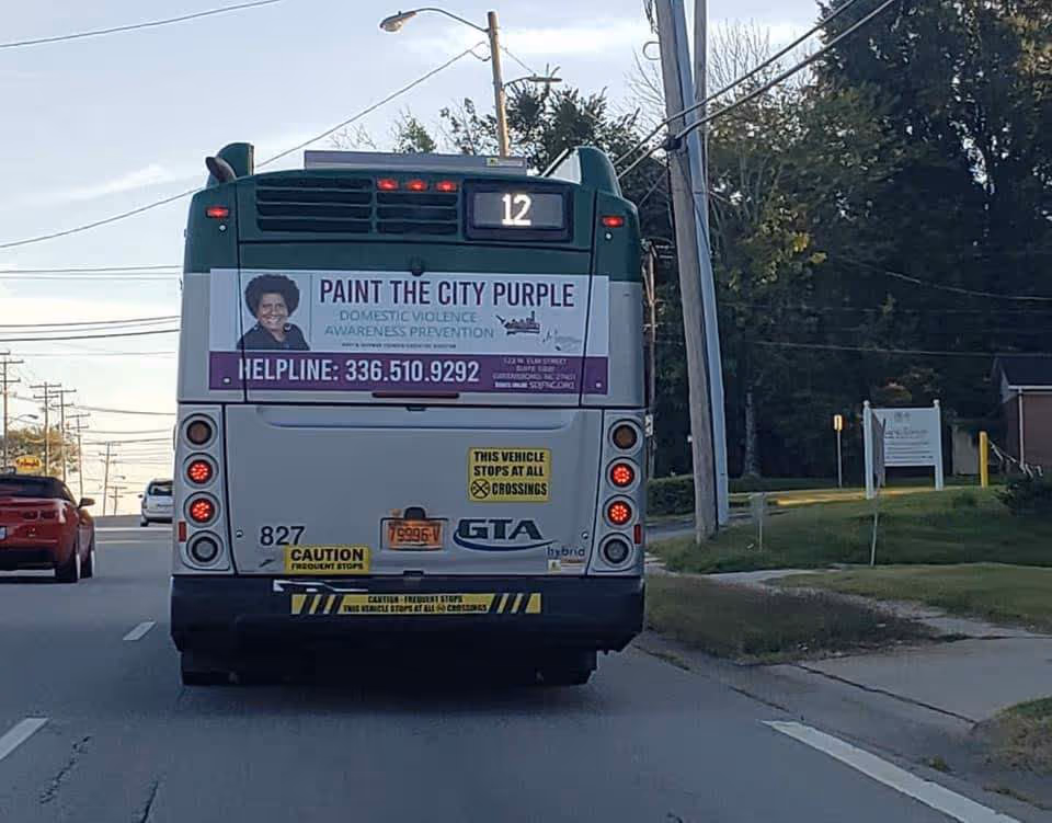 Rear view of a bus on a city street displaying a purple awareness ad.